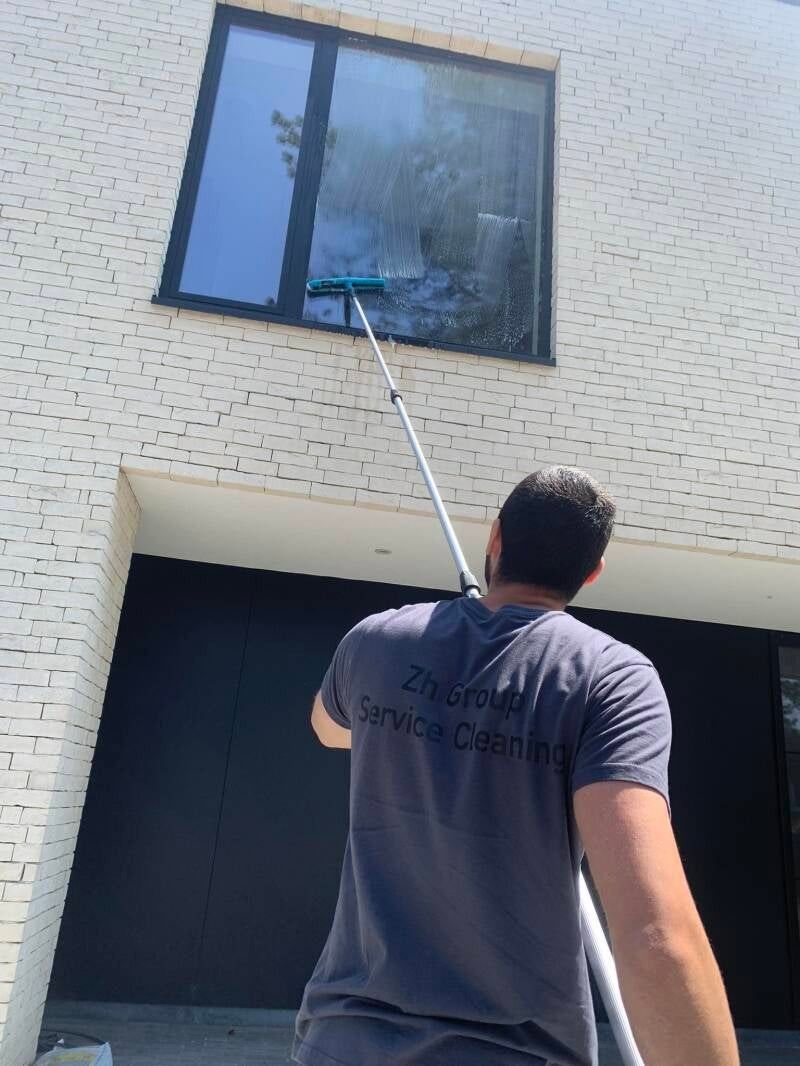 Medewerker van ZH Group wast een raam op de verdieping met een telescoopsteel